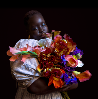 Fotografia de uma pessoa com um ramo de flores coloridas num ambiente de pouca luz.