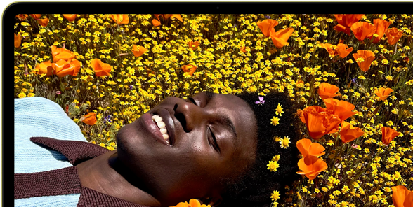 MacBook Neo na cor cítrico, o ecrã mostra uma pessoa a sorrir, deitada num campo de flores banhado pelo sol