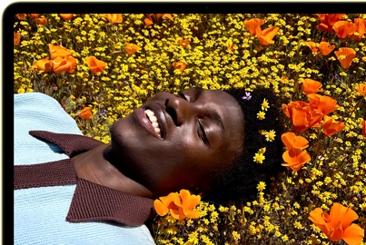 MacBook Neo na cor cítrico, o ecrã mostra uma pessoa a sorrir, deitada num campo de flores banhado pelo sol