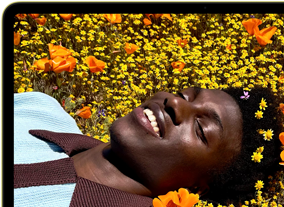 MacBook Neo na cor cítrico, o ecrã mostra uma pessoa a sorrir, deitada num campo de flores banhado pelo sol