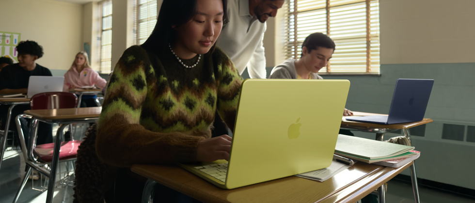Estudante a usar o MacBook Neo na cor cítrico, desligado da tomada a ser usado em contexto de sala de aula