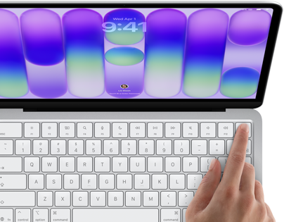 MacBook Neo na cor prateado, a mostrar o ecrã de início de sessão, o dedo de uma pessoa no sensor Touch ID no canto superior direito do teclado