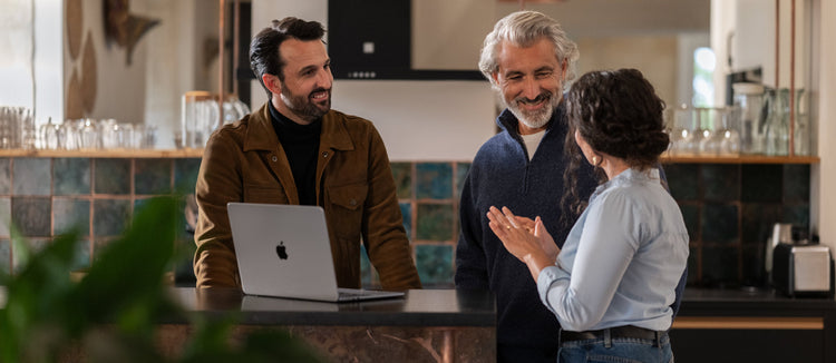 Três pessoas a conversar à volta de um MacBook num espaço de trabalho